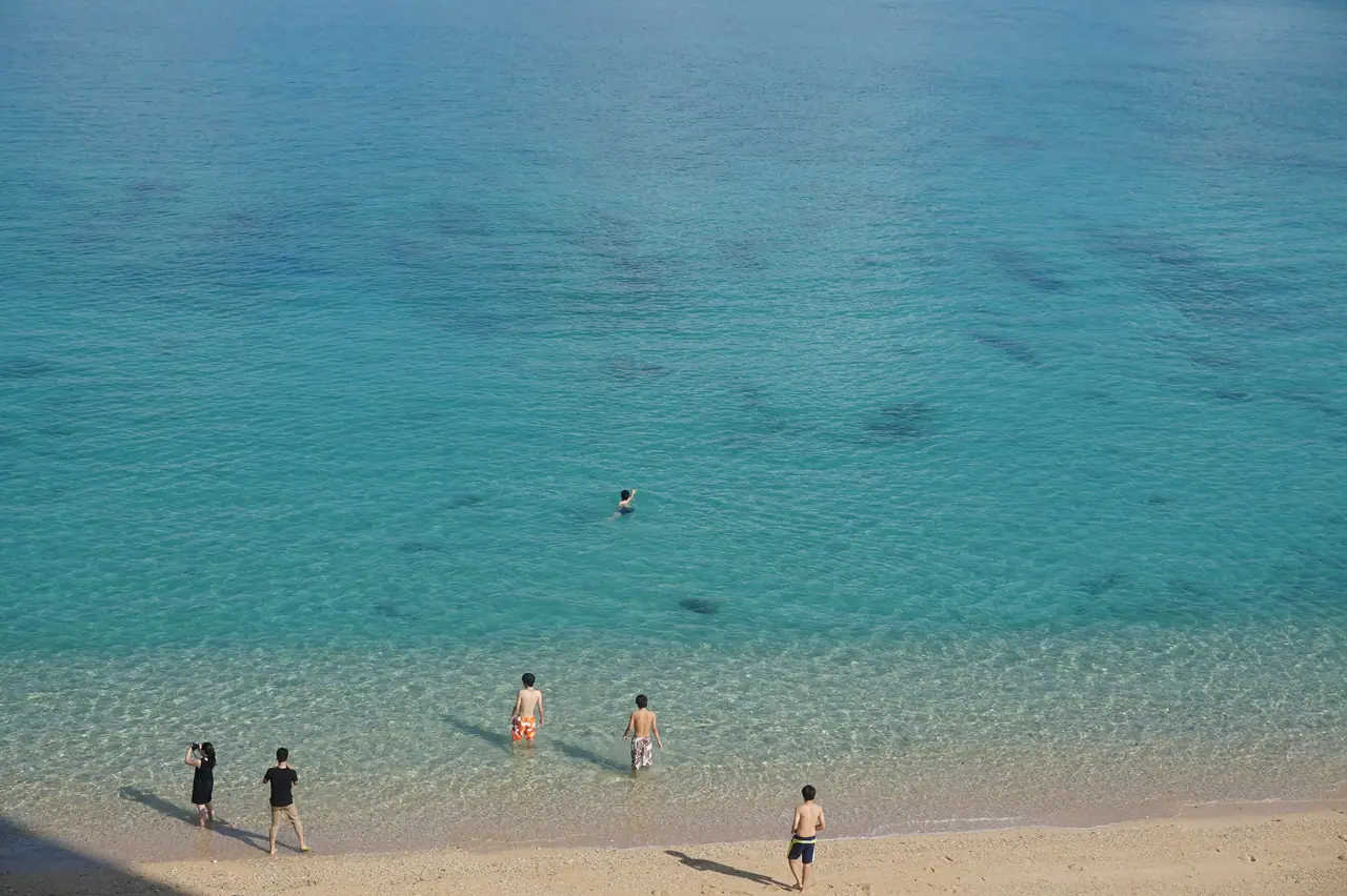 People swimming in clear turquoise water at an Okinawa beach